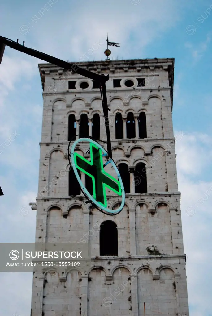 Steeple in the Old Town of Lucca with the typical greenly illuminanted cross for pharmacies in Italy in the foreground