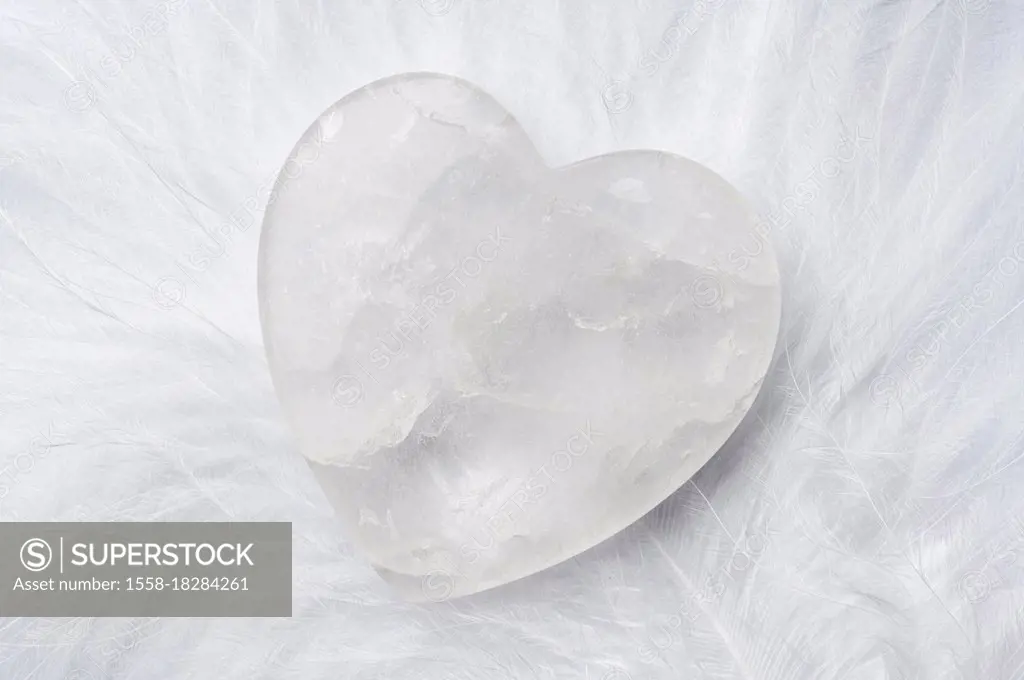 Rock crystal heart on white down feather, symbol of purity, innocence