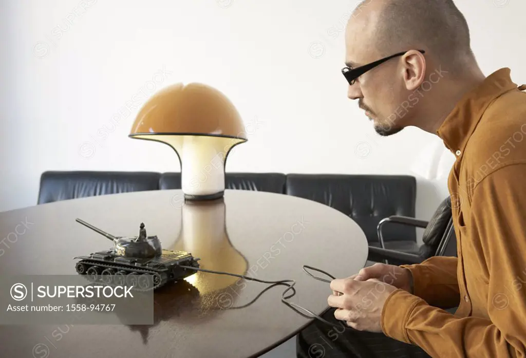 Sits man, table, tanks,,  , plays, profile,  broached,  20-30 years, glasses, glasses bearers, beard, Glatze, lamp, sofa, toy tanks, concentration, fa...