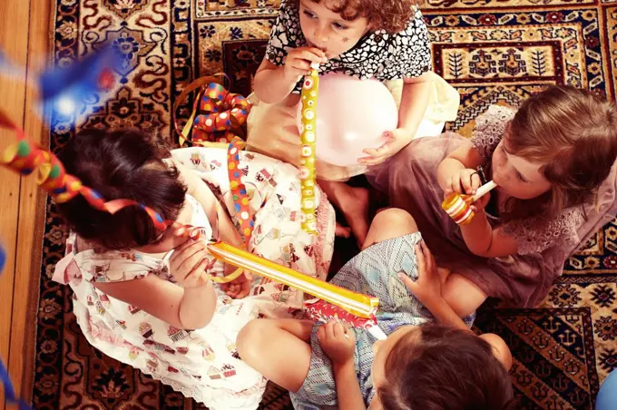 Party Girls sitting on a patterned carpet and blowing party horns