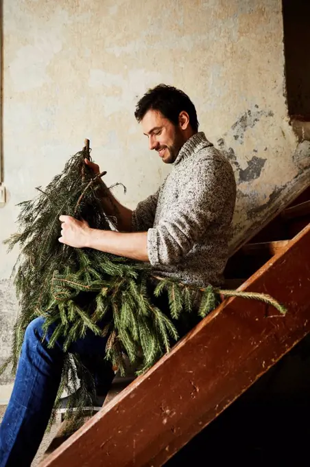 Man with knitted pullover, twigs of evergreens for decoration, stairs, sit, sitting, half-portrait, side view,