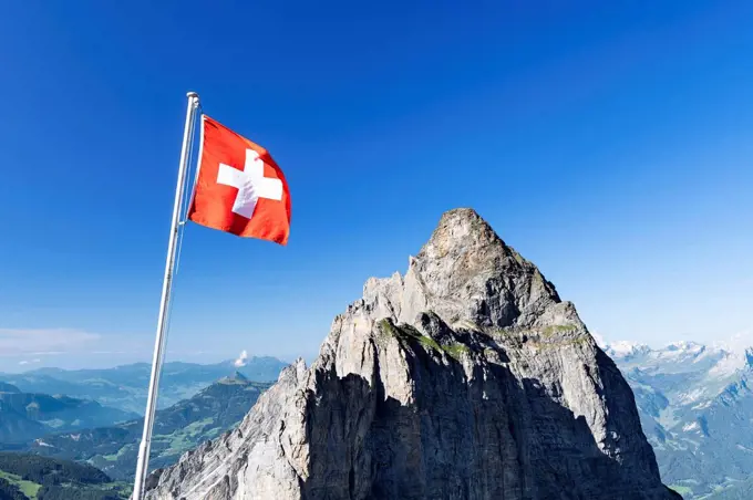 Swiss flag with Gstellihorn under a blue sky on a sunny summer day. Bernese Alps, Canton of Bern, Switzerland
