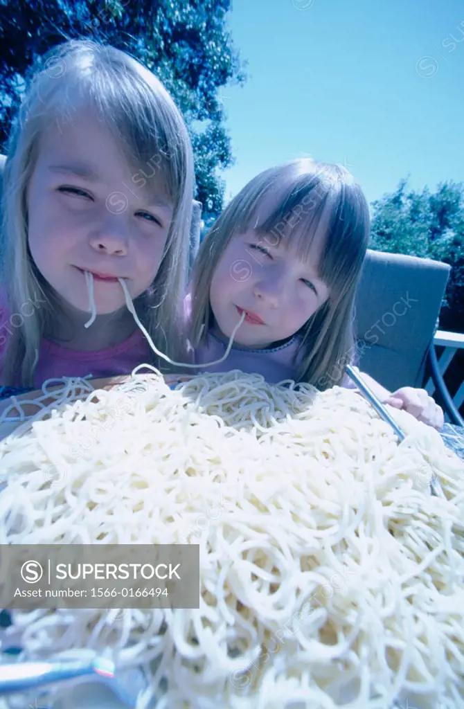 Twins eating a gigantic bowl of spaghetti