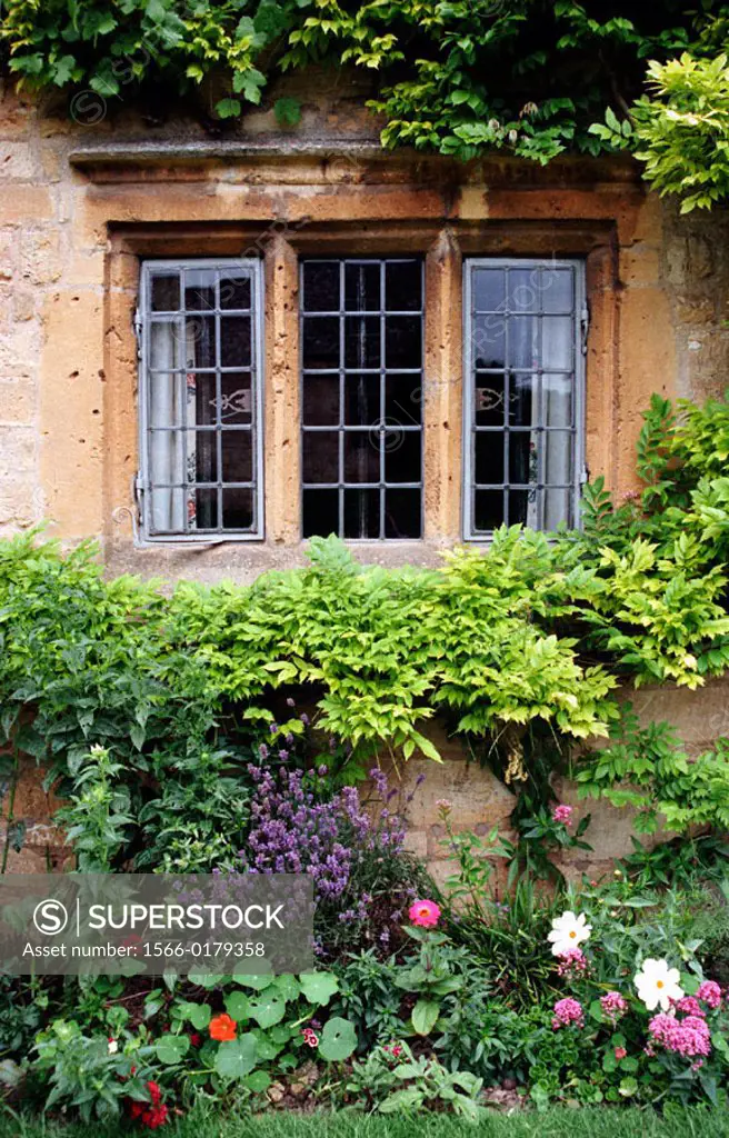 Flower garden framing the wrought iron window of a stone house in Chipping Campden, in the Cotswolds region of England