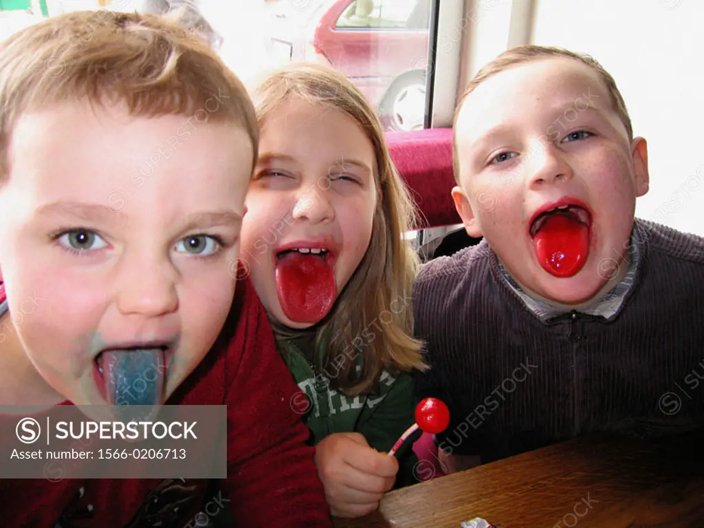 Three boys, aged 4 and 8, show off their colored tongues while sucking on flavoured lollipops