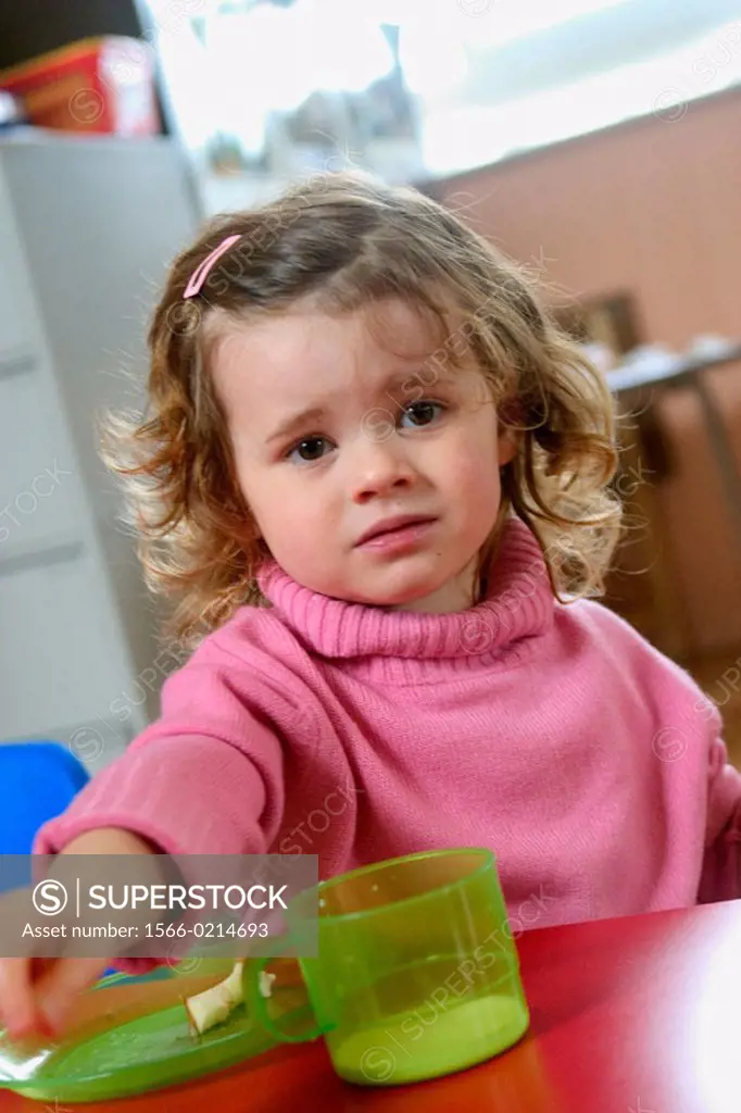 Three year old girl with a plate and cup, looking miserable