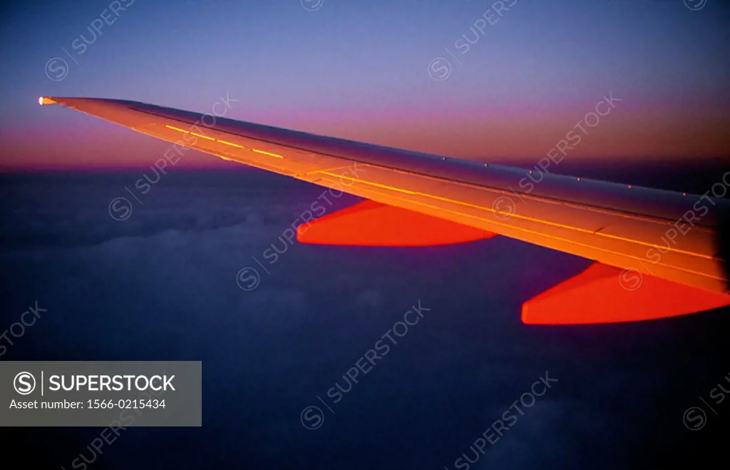 Airplane wing shot out window at sunrise.