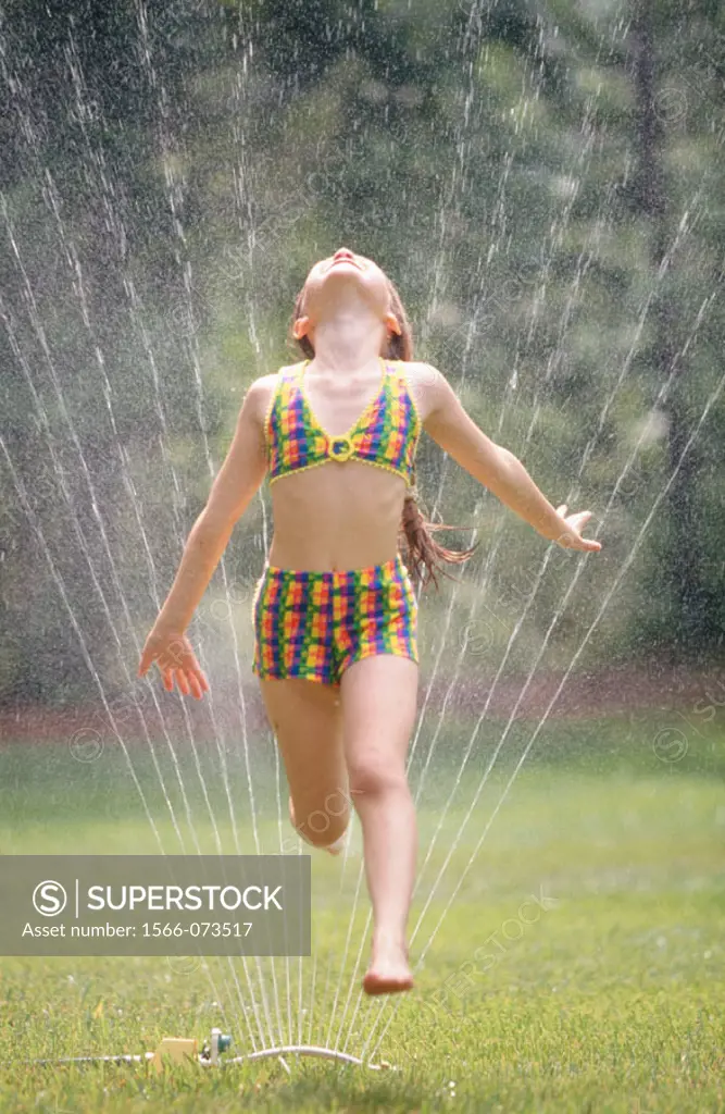 Girl running through lawn sprinkler on summer´s day.