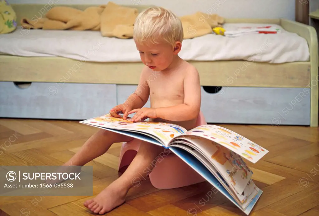 2 year old boy sitting on the pot and looking at a picture book