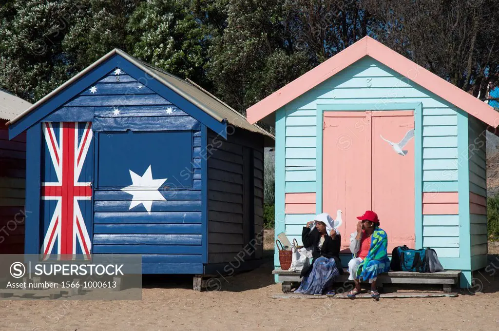 People sitting on the steps of the Victorian-era bathing boxes at Brighton Beach on the shores of Port Phillip Bay, Melbourne, Australia