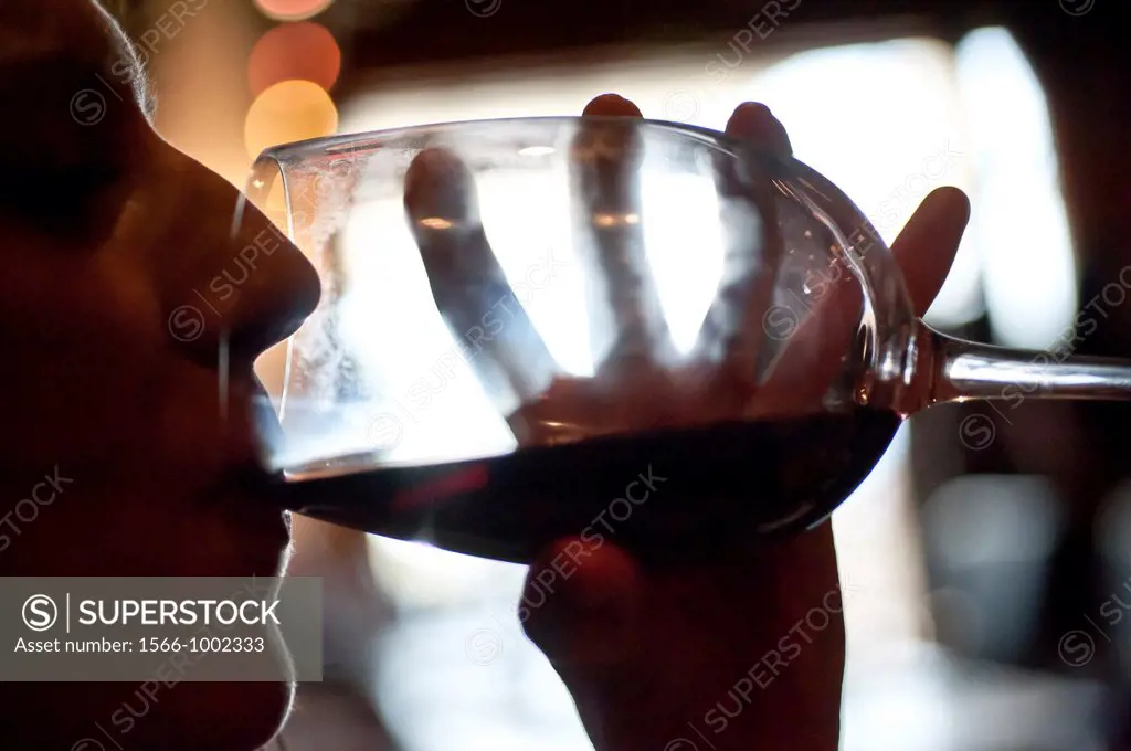 Silhouette of fingers and face of a wine glass of a woman drinking wine