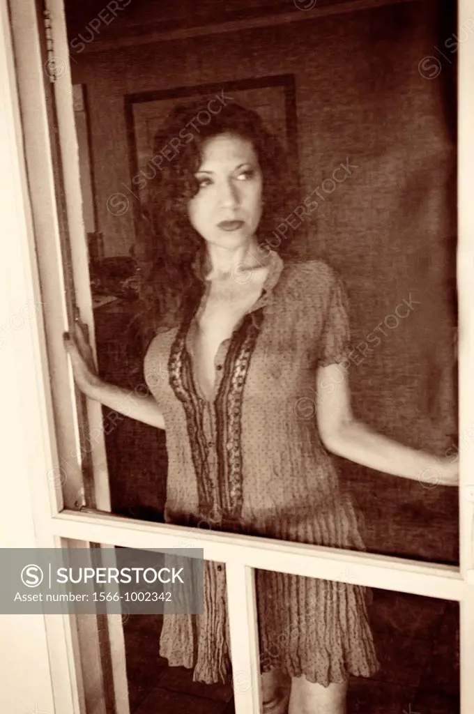 Portrait of a 42 year old woman with long curly black hair wearing a sheer dress looking away from the camera in a provocative pose standing behind a ...