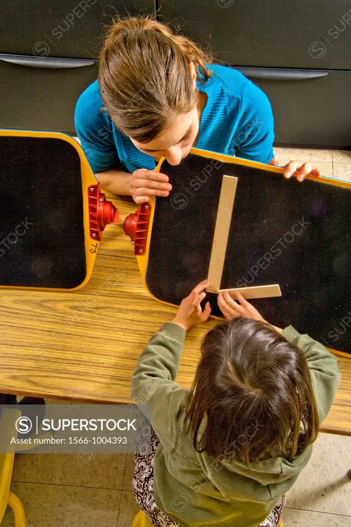 A teacher guides a blind child´s hands to form the letter ´L´ by touch using two sticks in a special needs pre-Braille writing class at the Blind Chil...