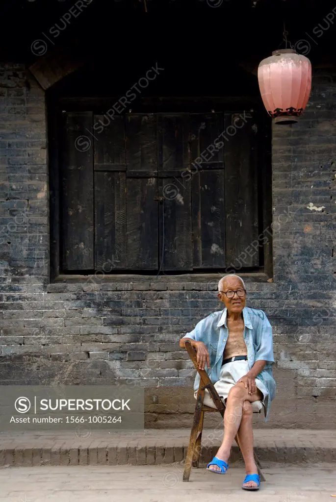 Old Chinese man sitting in of the traditional Streets of Pingyao, Shaanxi Province, China.