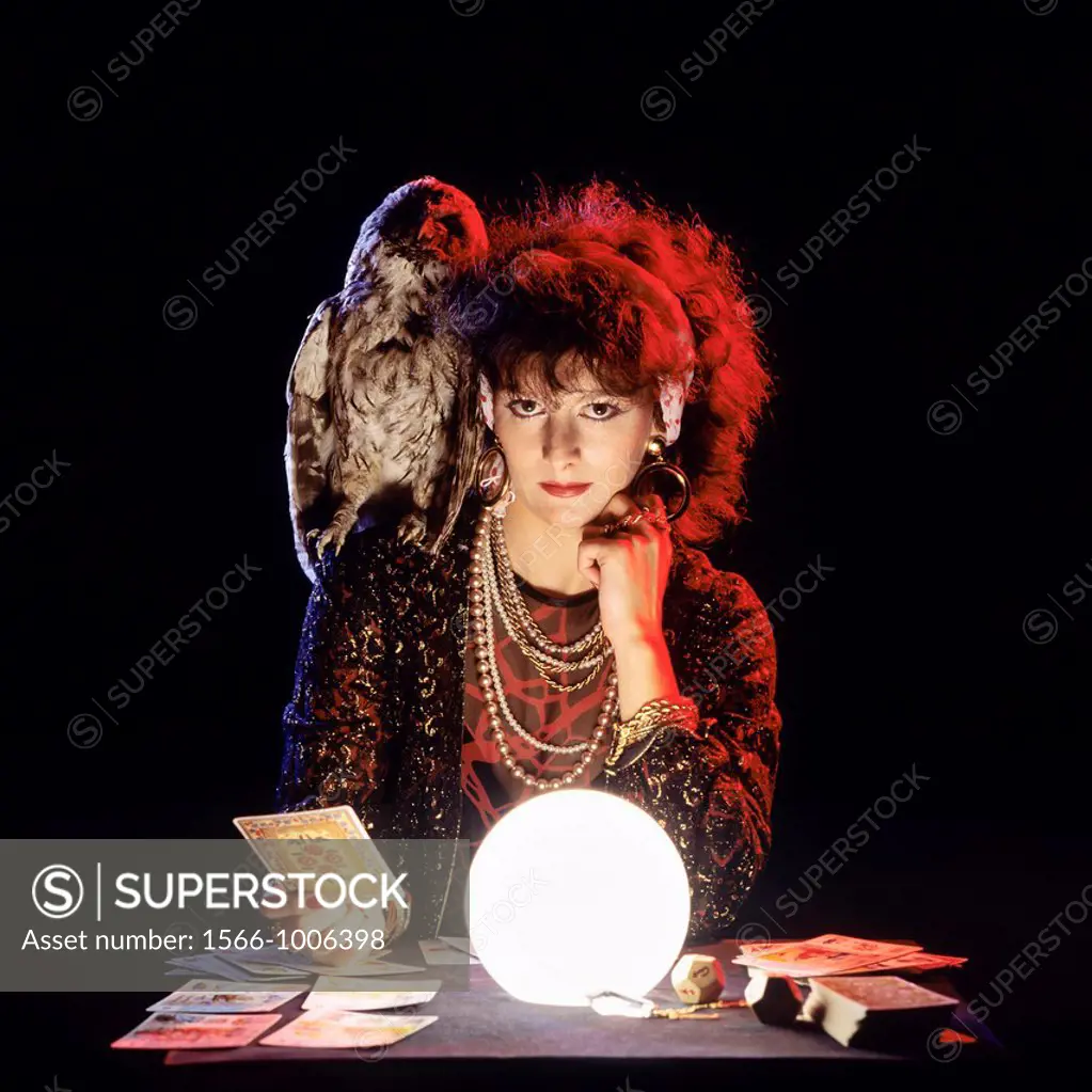Gipsy fortune teller with an owl on her shoulder, tarot cards and lit crystal ball