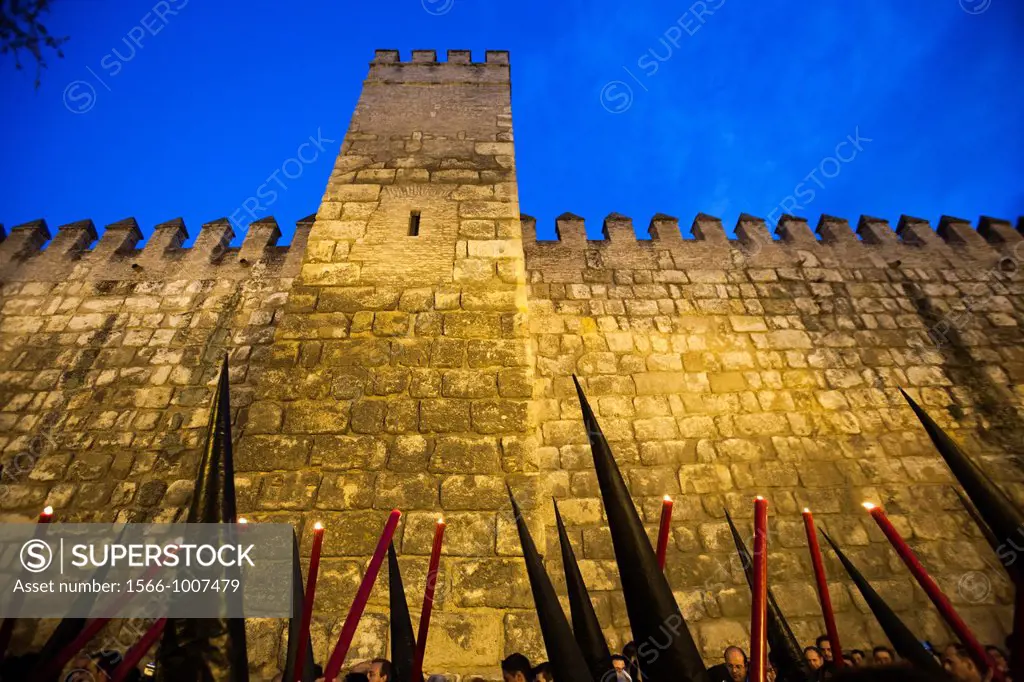 the cones of hooded penitents bearing candles against the Alcazar ramparts, Holy Week, Seville, Spain