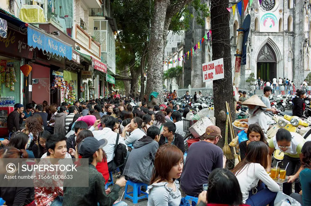 A crowd of people sitting in the streets front of an outdoor cafe with the old St  Joseph´s Cathedral in the background