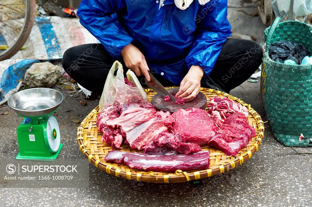 A woman selling raw pieces of meat and fish on a sidewalk in Vietnam