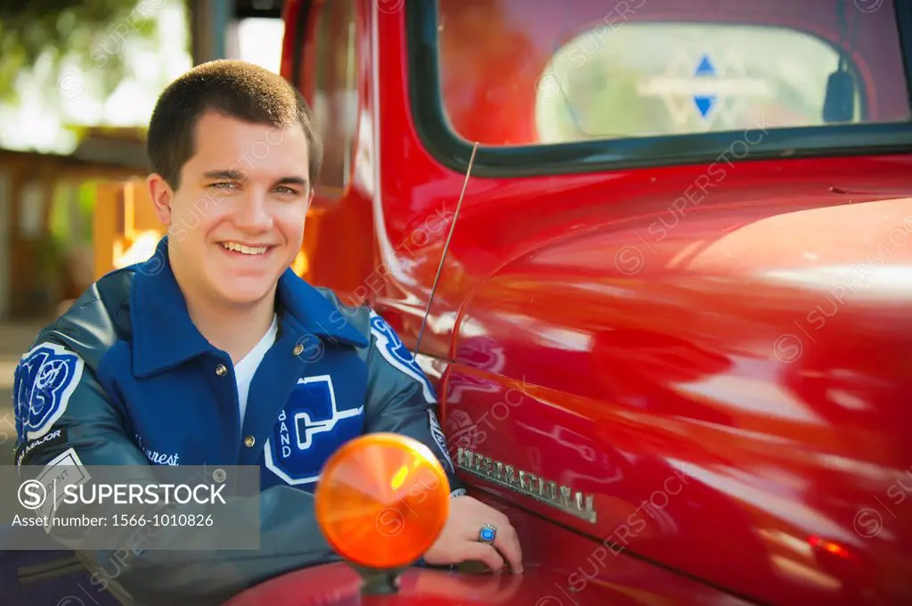 Highschool senior, male caucasian, 17 years old, posing with his school letterman jacket next to vintage automobile