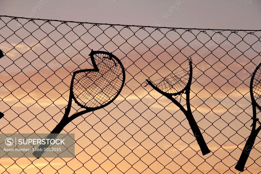 Old broken tennis rackets tied to fence at tennis club