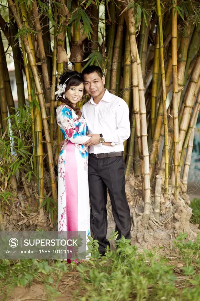 A formally dressed couple having their portrait taken in front of a small bamboo grove