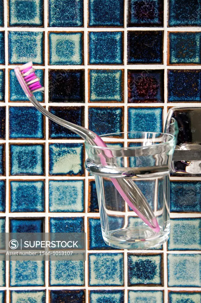 toothbrush in the glass against wall covered with ceramic tiles
