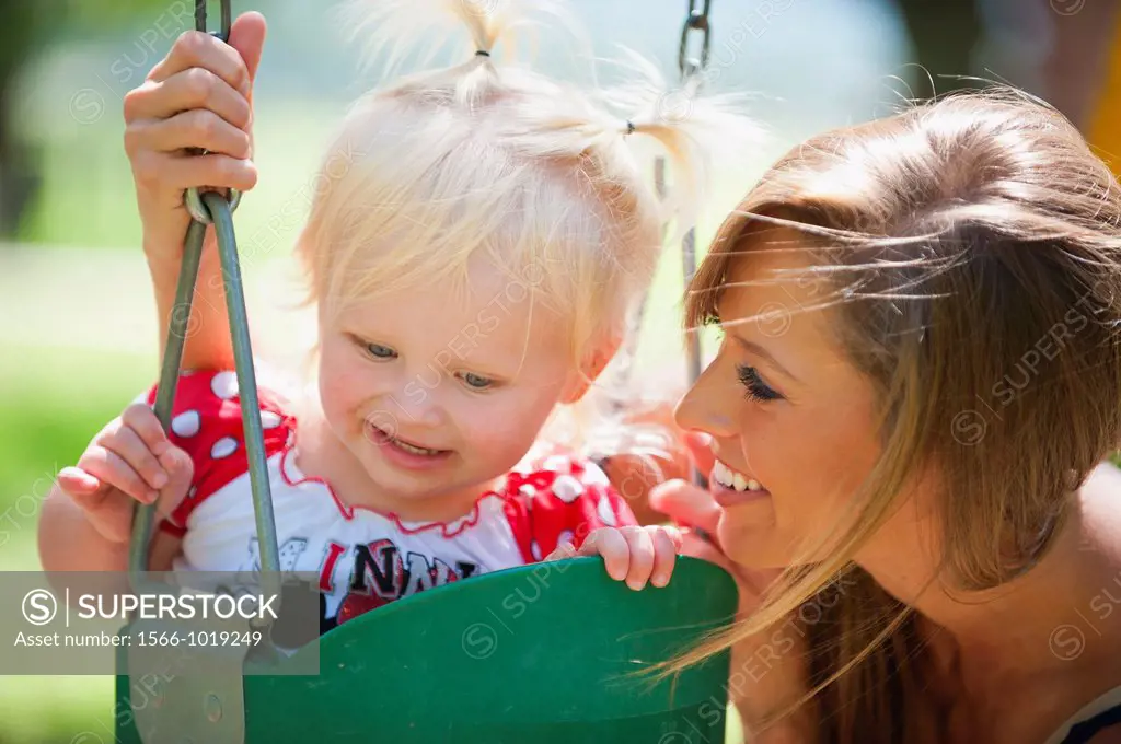 Young mother with two years old female child on a swing in a park