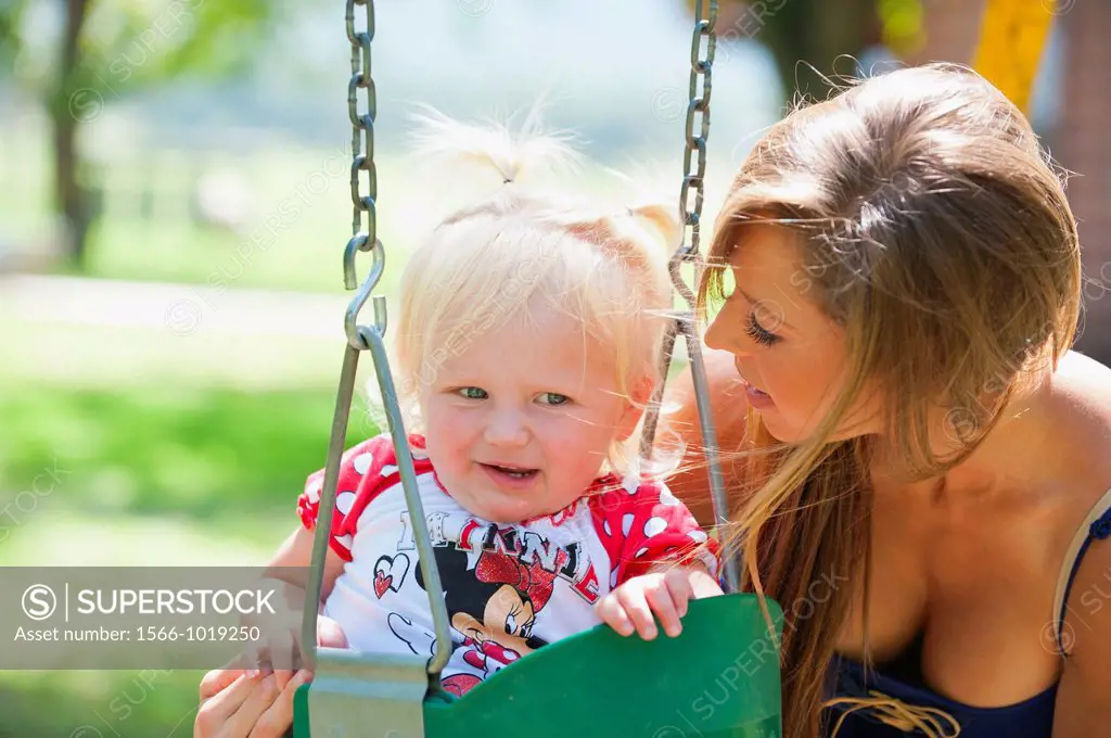 Young mother with two years old female child on a swing in a park