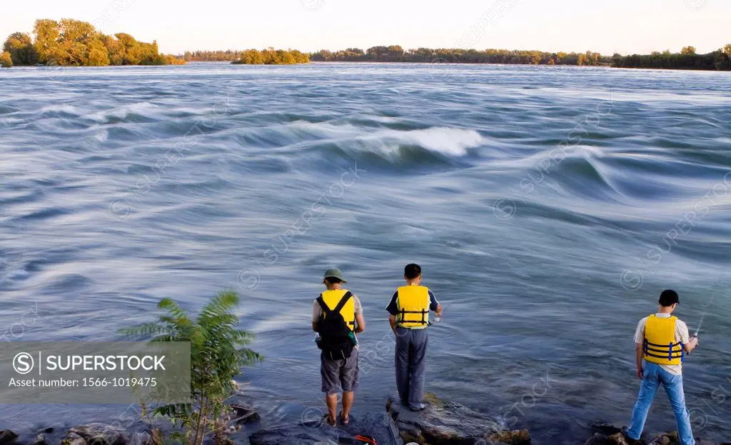 Fishermen wearing yellow lifesaving jackets fishing in Saint Lawrence, Montreal, Canada