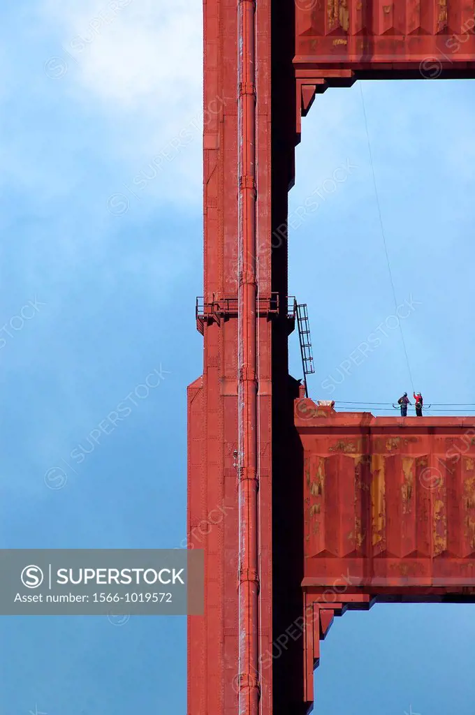 Two workers stand on the north tower of the Golden Gate Bridge