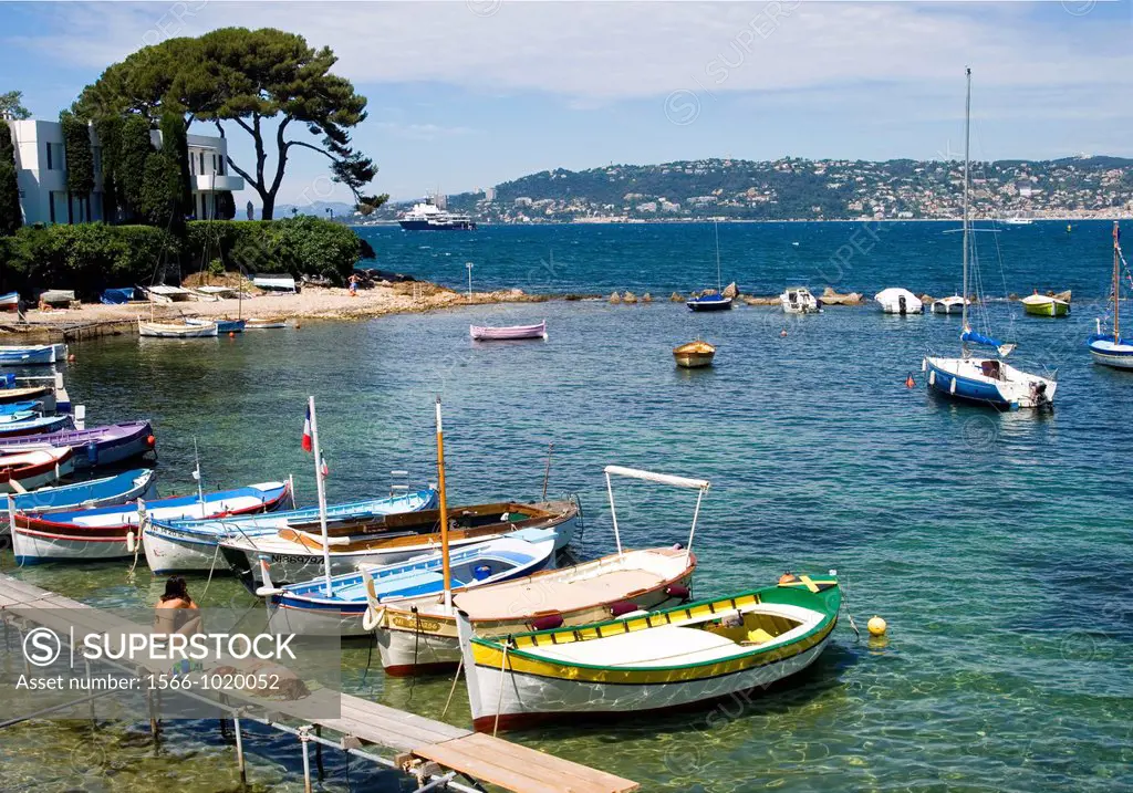 Cap d Antibes, South of France, Small picturesque bay with colourful boats and pine trees  Two young ladies sunbathing