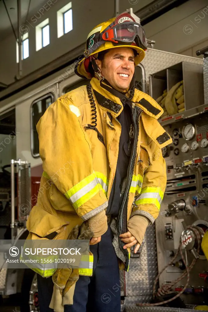 Wearing his helmet, a young firefighter dons his yellow safety jacket at a firehouse in Laguna Niguel, CA  Note fire engine pumper in background A you...
