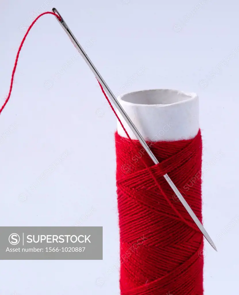 A reel of red cotton with a threaded needle held in place through the thread