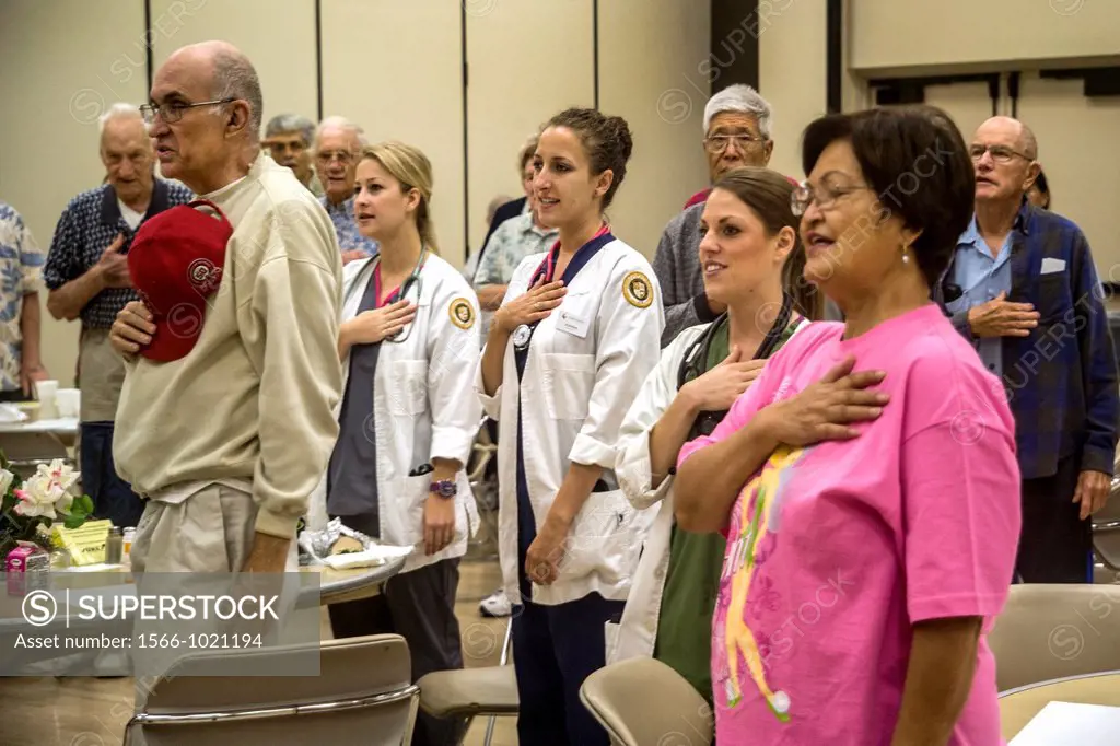 Medical personnel join senior citizens in the Pledge of Allegiance before lunch at a senior center in Tustin, CA