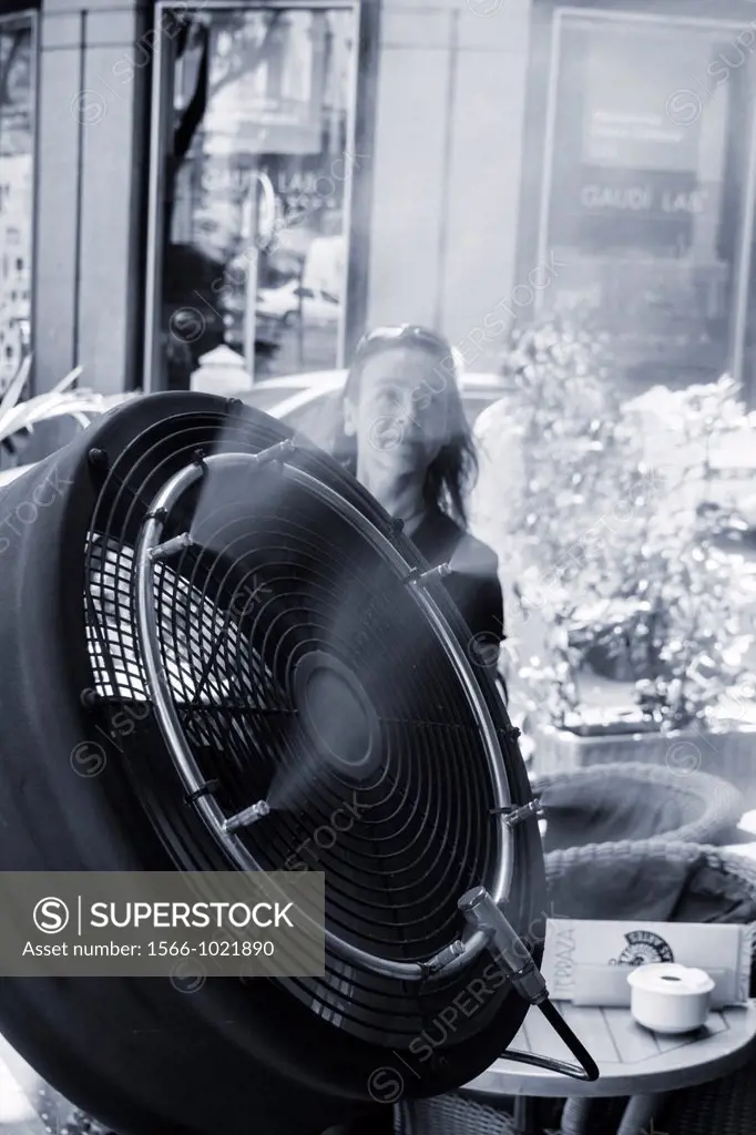 Woman cooling off near fan spraying fine water mist at street cafe in Madrid, Spain