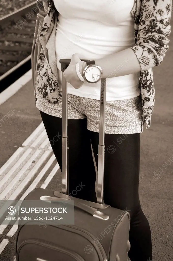 young woman with suitcase waiting on railway platform with well seen hand watch, Cornavin - the main railway station in Geneva, Switzerland