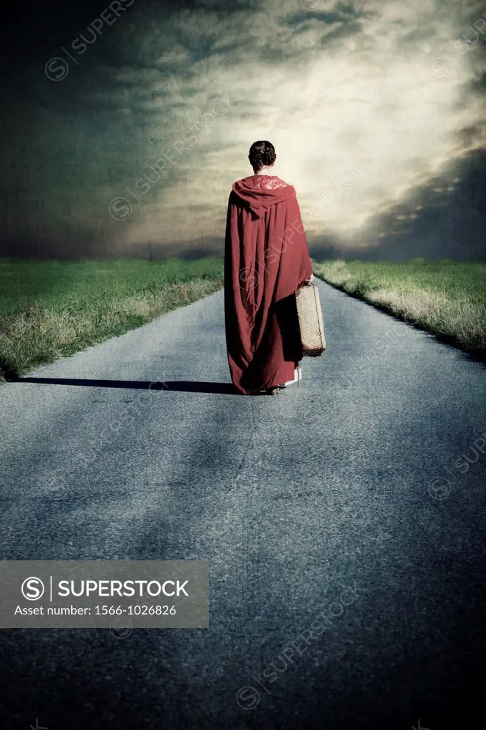 a woman in a red cape is walking along a road with a suitcase