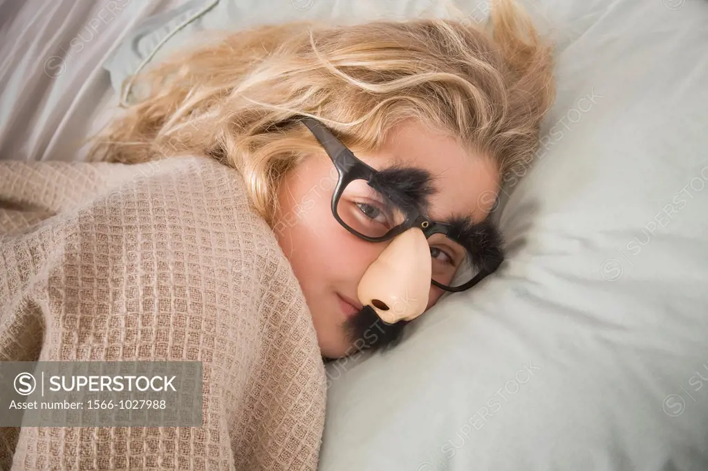 Young blonde girl in bed, wearing funny glasses