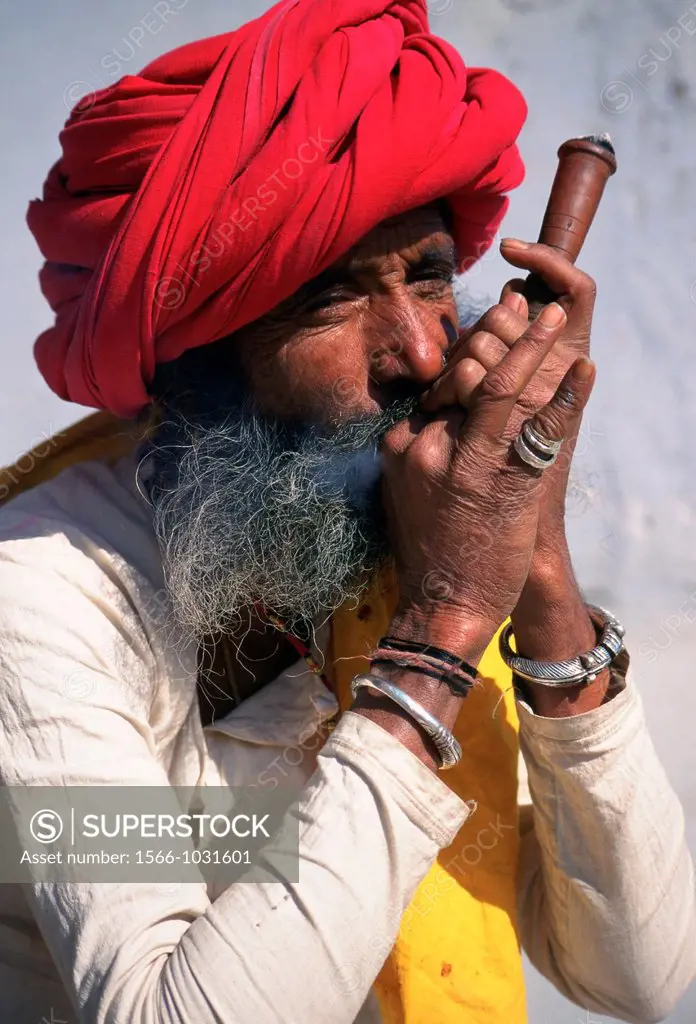 Hindu man smoking opium with his pipe. He belongs to the Rebari caste. Rajasthan, India.