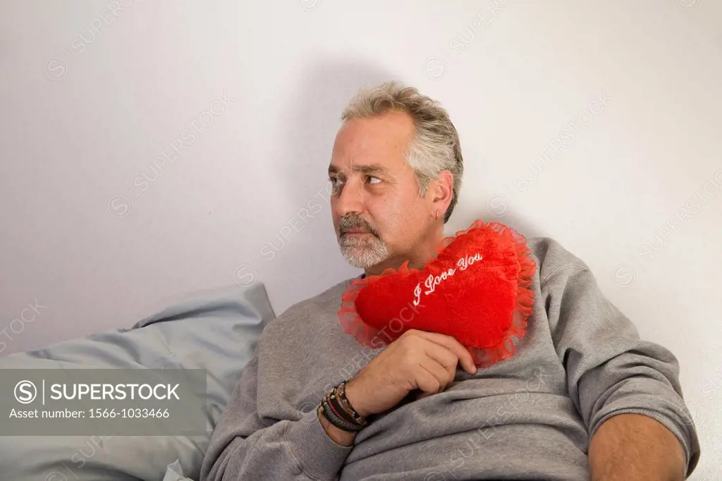 Middle-age man holding a heart-shaped pillow with ´I Love You´ written on it