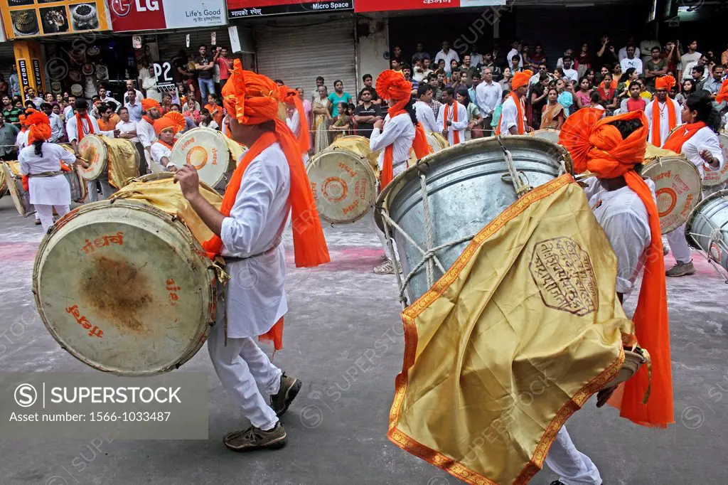 Indian girls & men wearing headgear called feta and white kurta pajamas and playing musical instrument called ´dhol-taash´ during Anant Chaturdashi Ga...