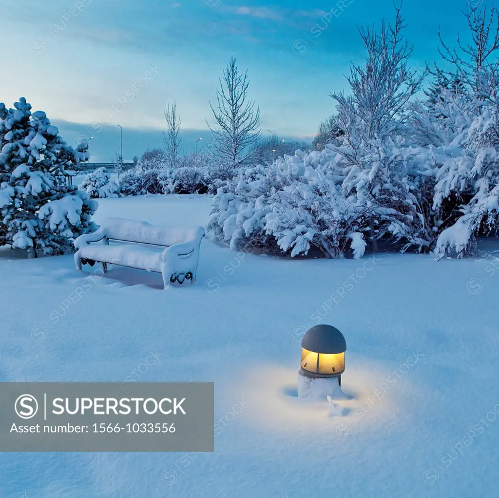 Snow covered bench, light and trees in park near Reykjavik, Iceland