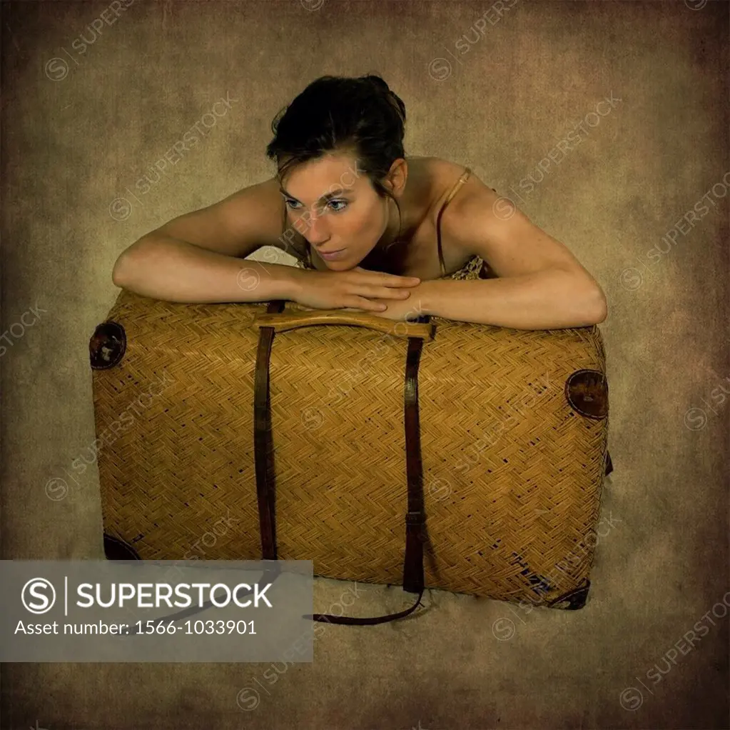 a young woman leans on an old suitcase