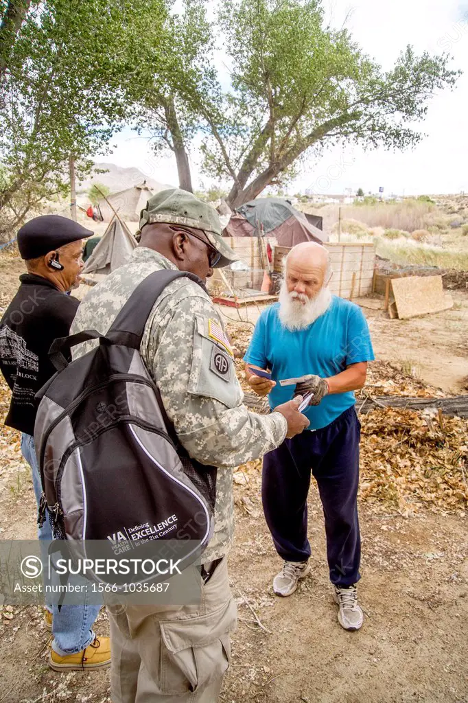A uniformed African-American U S  Army reservist offers a homeless military veteran information on Veterans Administration free medical care at an out...
