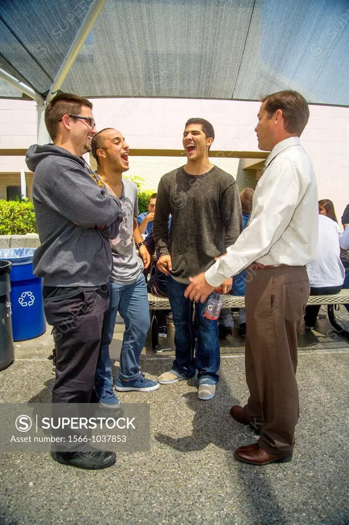 A high school principal talks with three male senior students on the suburban campus at lunchtime in Aliso Viejo, CA