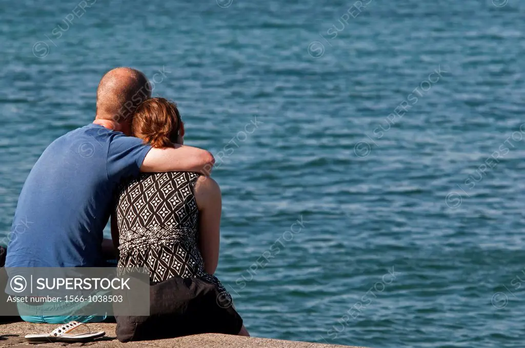 Embracing couple sitting in front of Geneva Lake, Geneva, Switzerland