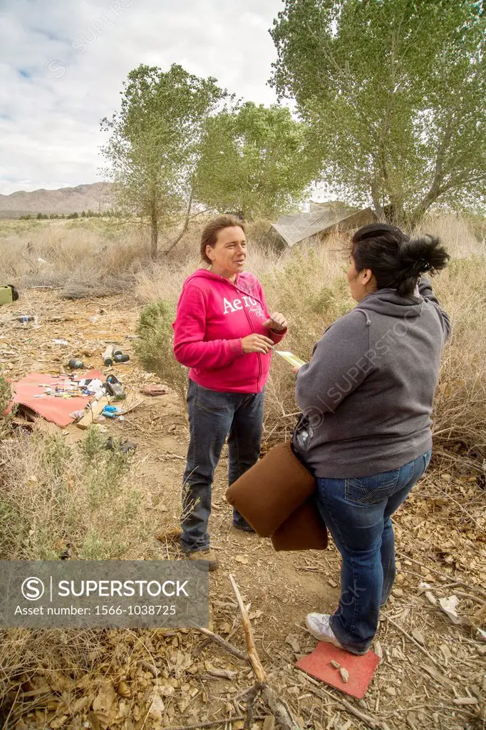 A social worker talks with a homeless woman living in an outdoor encampment in Victorville, CA  Note brochure with housing information being given