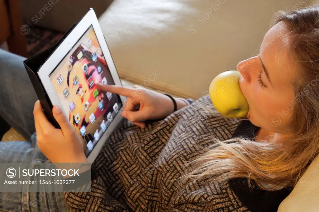 Twelve years old girl relaxing with a tablet computer and with an apple in her mouth