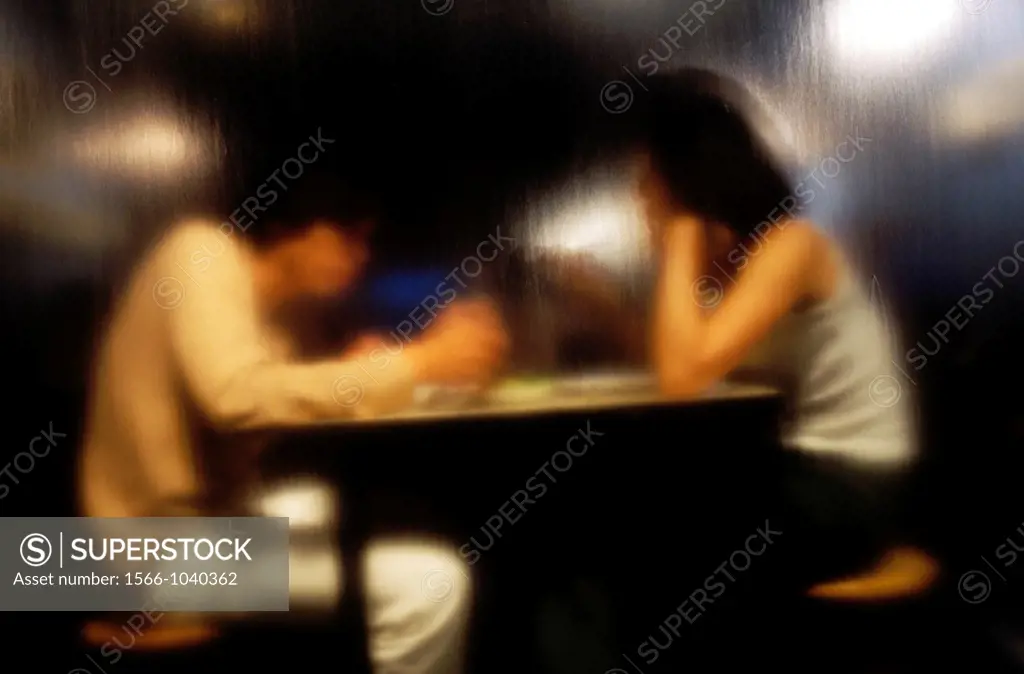 Two young Asians eating, photographed through glass, runs down to the water.