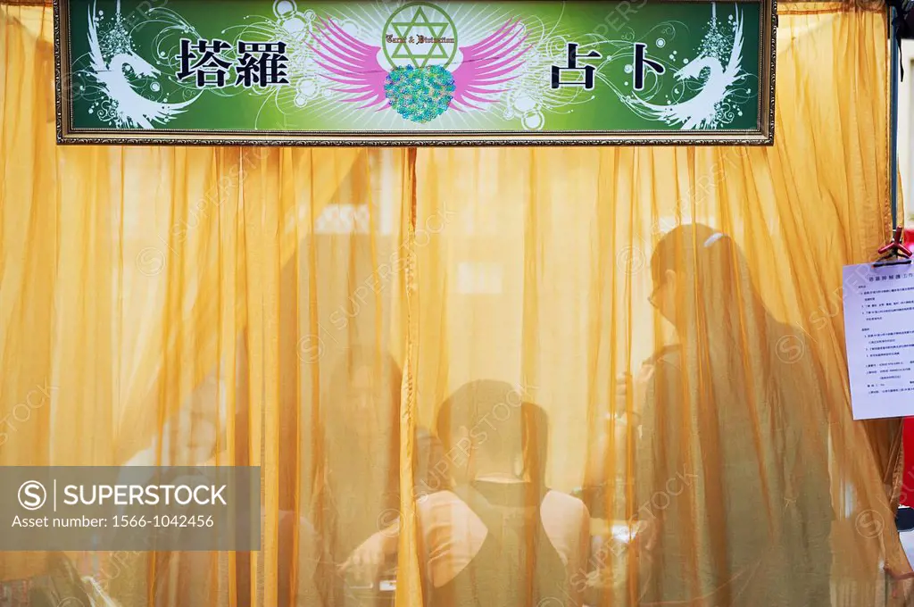 A tarot card reader at a makeshift booth covered in a sheer fabric